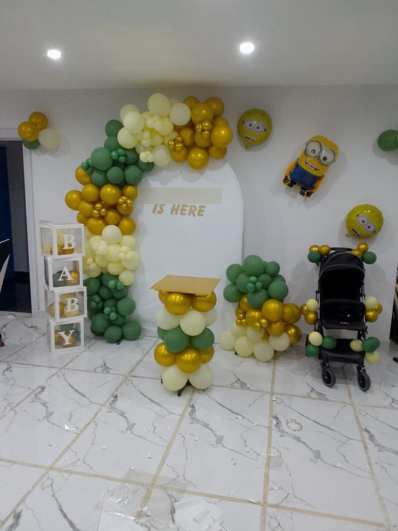 Green, gold and cream balloon arch with BABY blocks, minion balloons and a stroller – Events In Sialkot