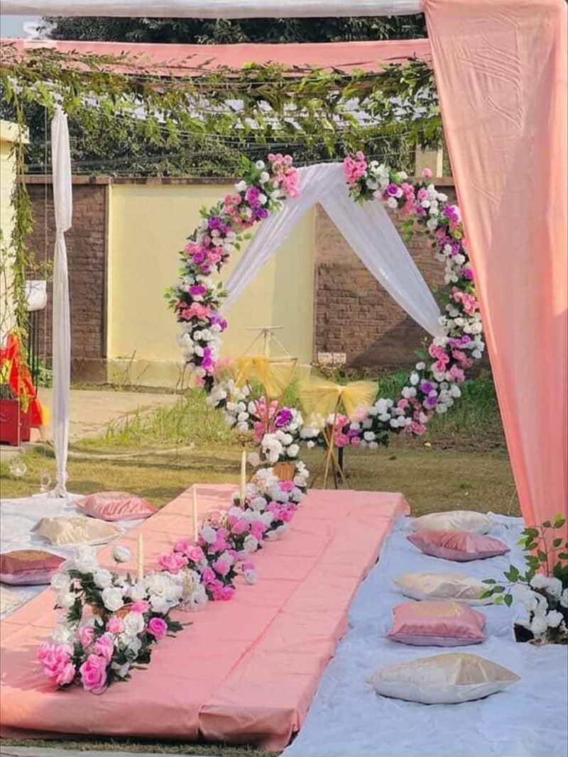Floral ring backdrop with pink drapes and cushion seating in a garden – Events In Sialkot