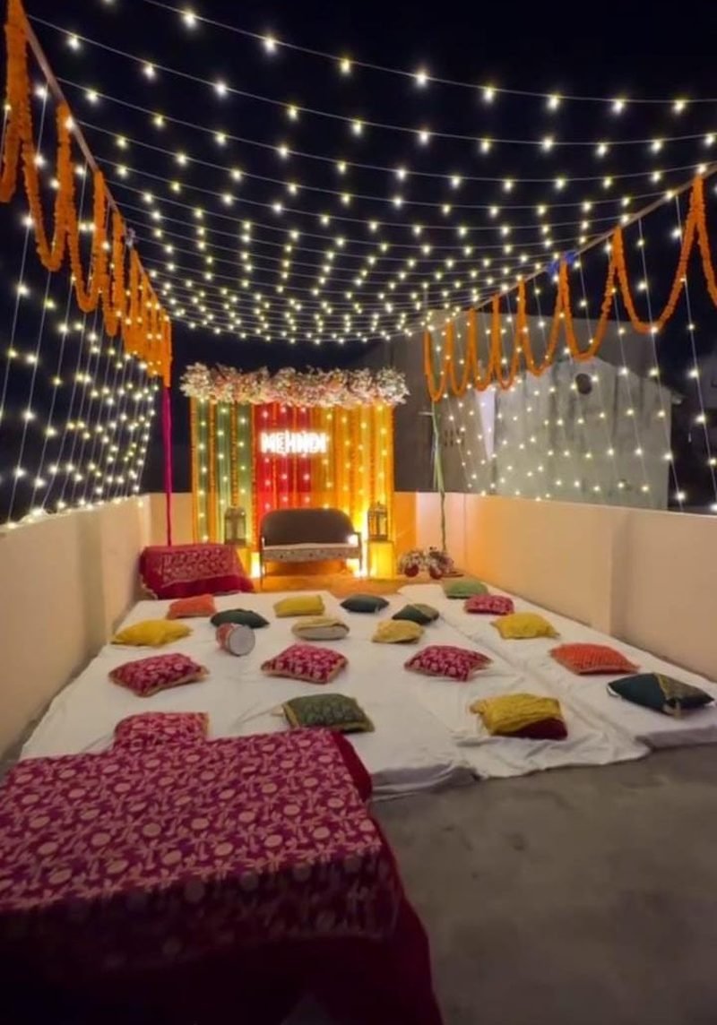 Rooftop mehndi setup at night with fairy-light canopy, marigold garlands and neon sign – Events In Sialkot
